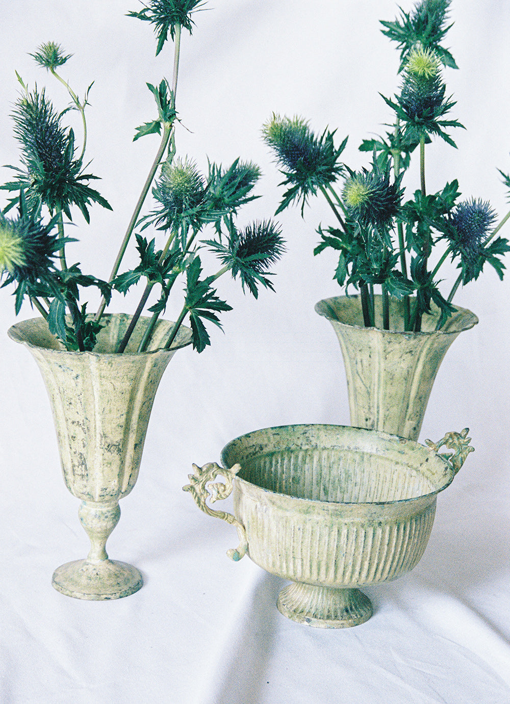 Three pale green tole planters, a footed urn between two trumpet vases