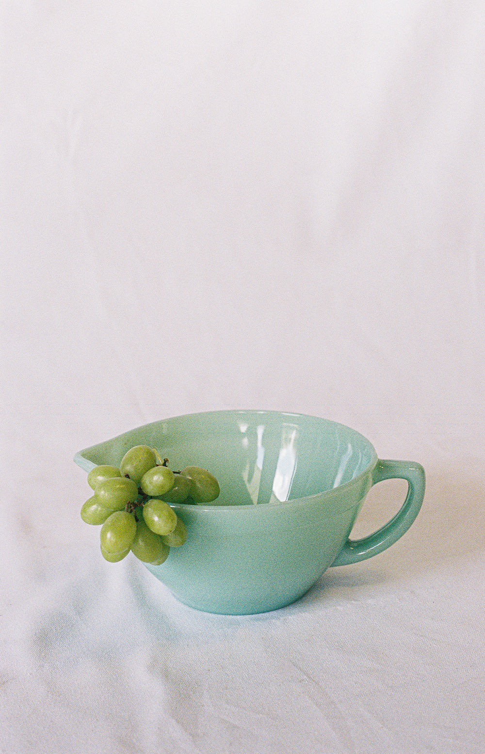 Jadeite glass mixing bowl with a handle and pouring spout, holding grapes