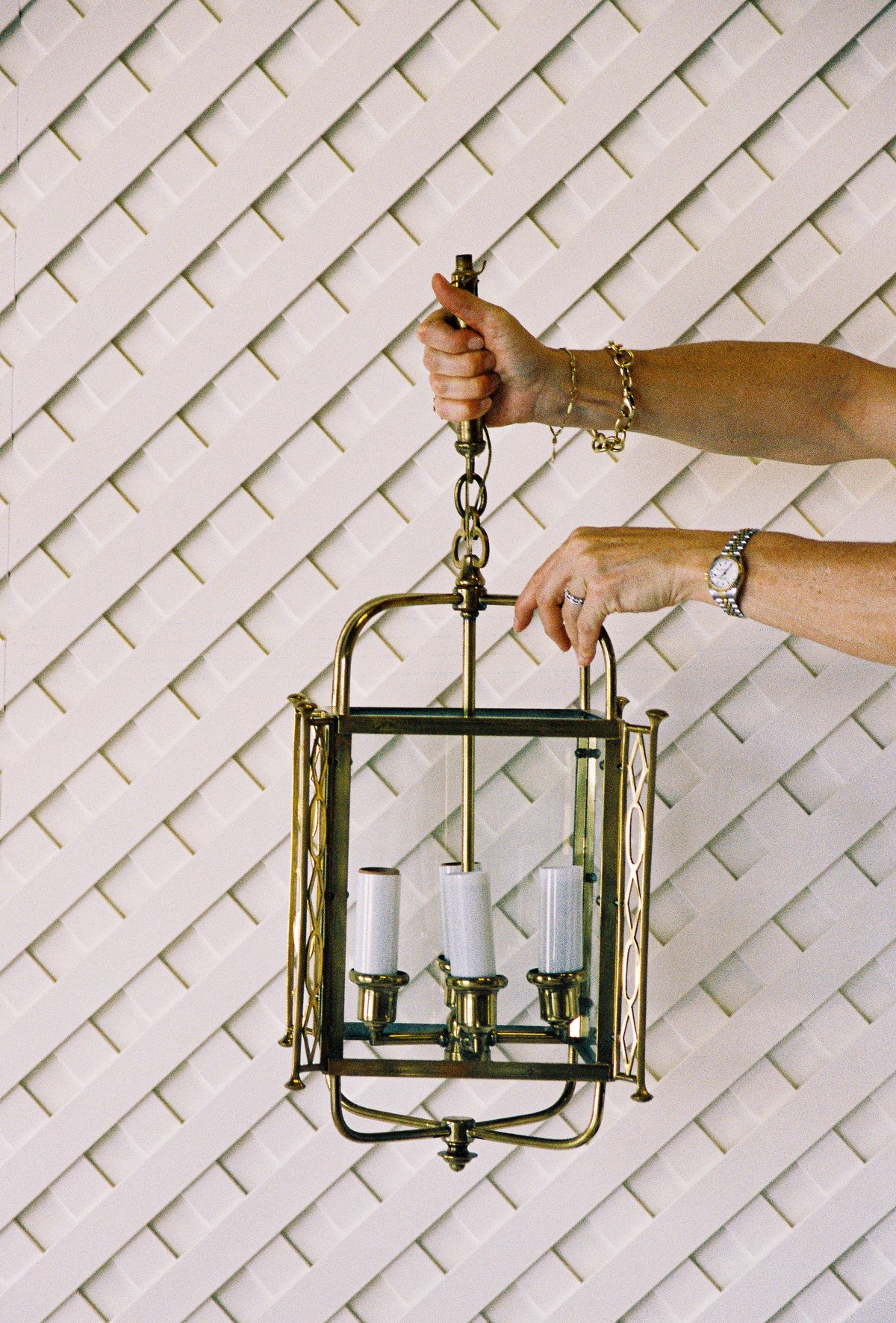 Hands opening the glass door of the brass lantern to show its four candle lights