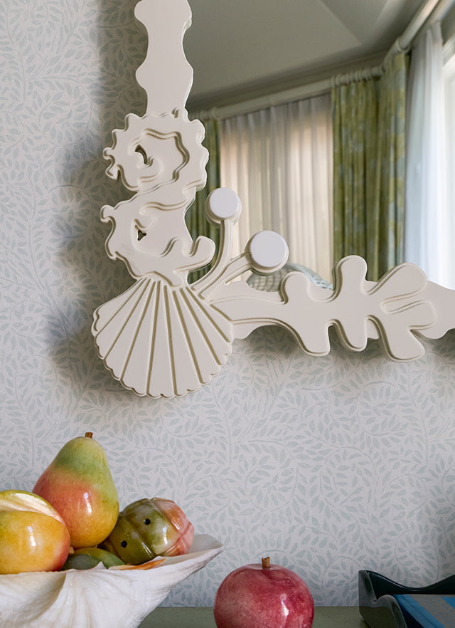 White sculpted mirror frame above a shell bowl of pears and pomegranates