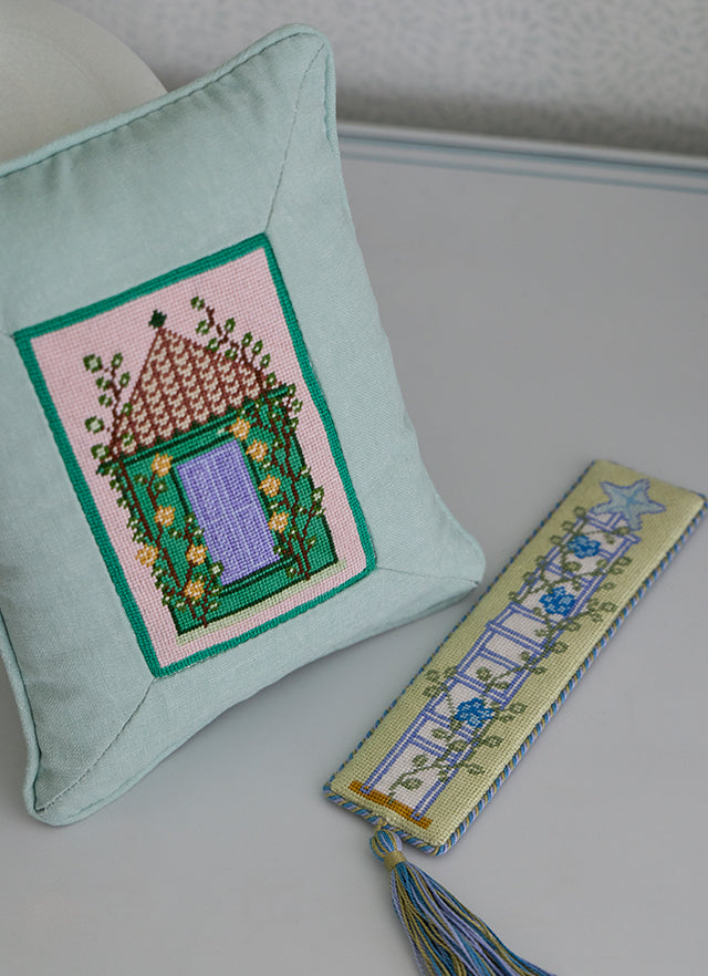 Needlepoint pillow of a green garden folly beside a matching needlepoint bookmark with a tassel