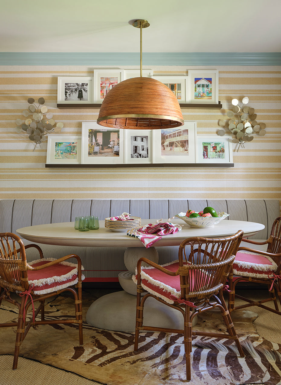 Breakfast banquette with rattan chairs, a woven pendant and framed prints on a striped wall