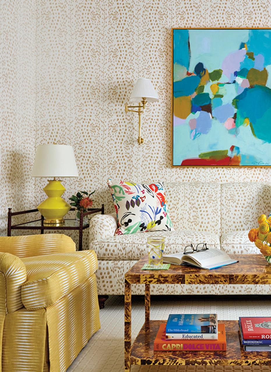 Sitting room with a yellow striped armchair, a tortoiseshell coffee table and an abstract painting above a patterned sofa