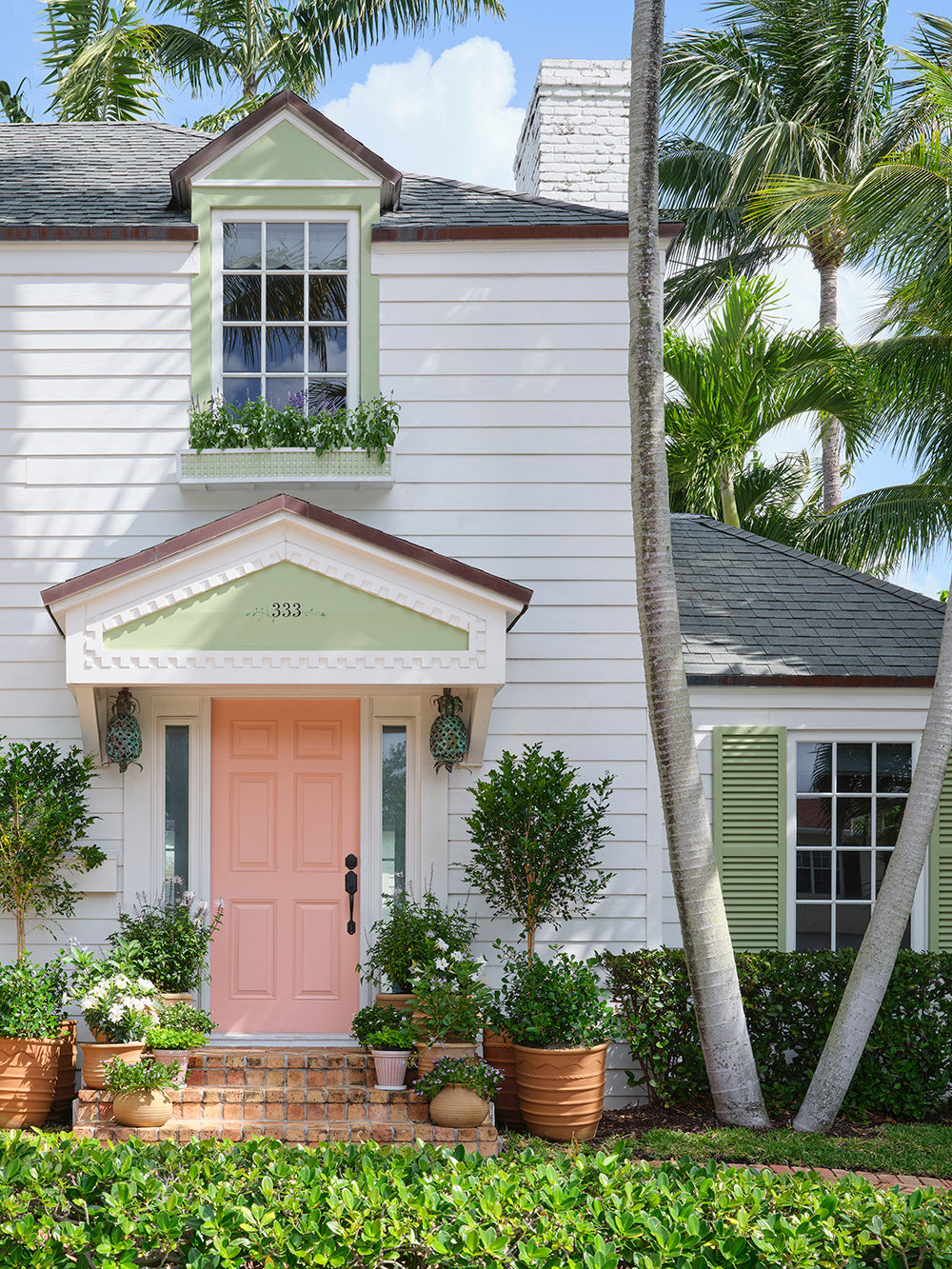 Front of the white house with a pink door, green shutters and potted plants