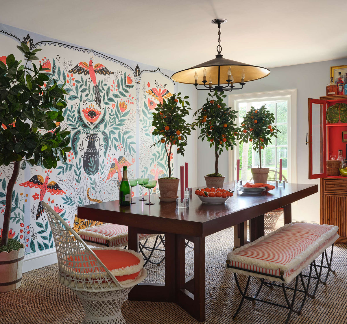 Dining room with a painted bird and floral mural, potted orange trees and a dark wood table