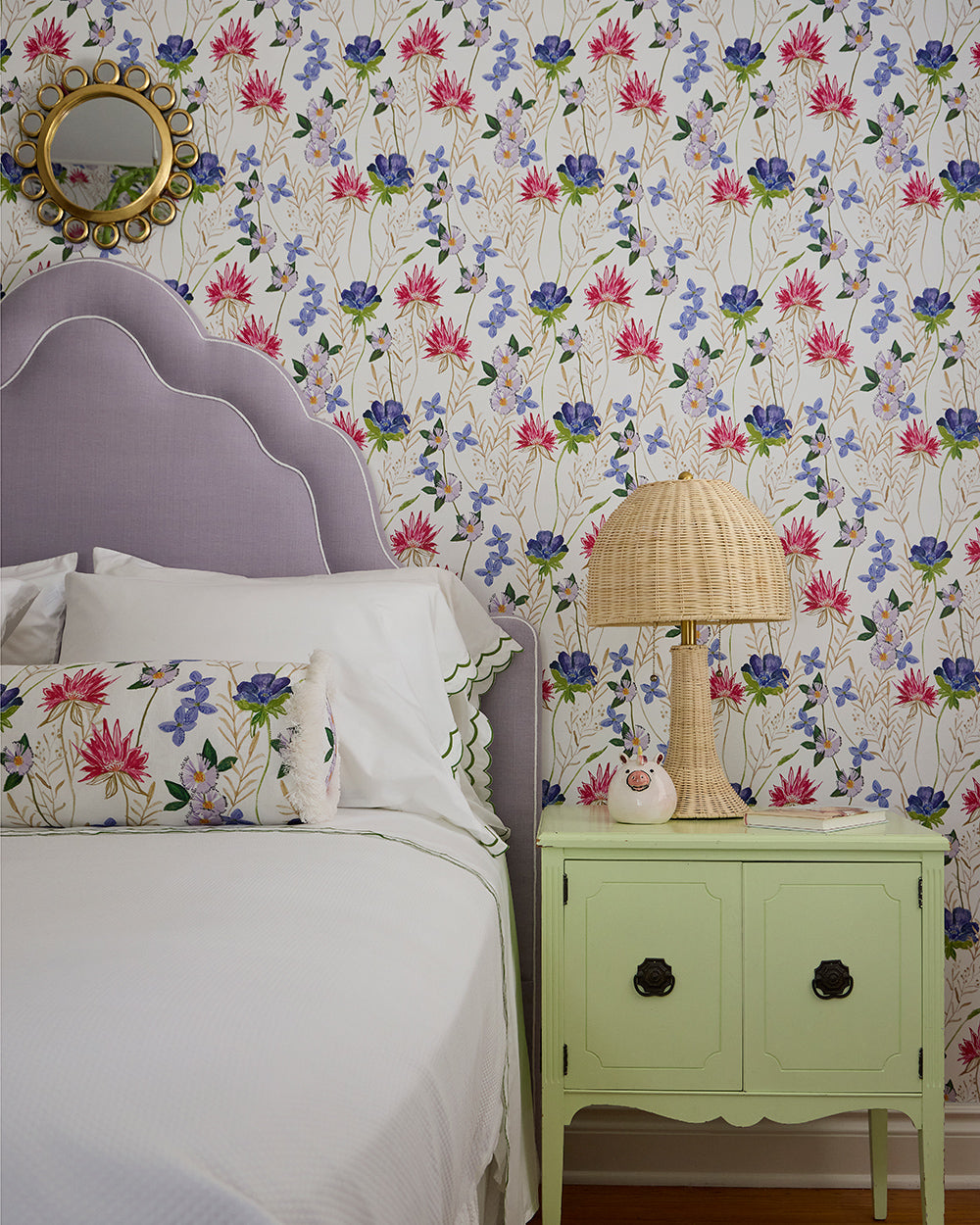 Lilac headboard and a green nightstand with a rattan lamp against floral wallpaper