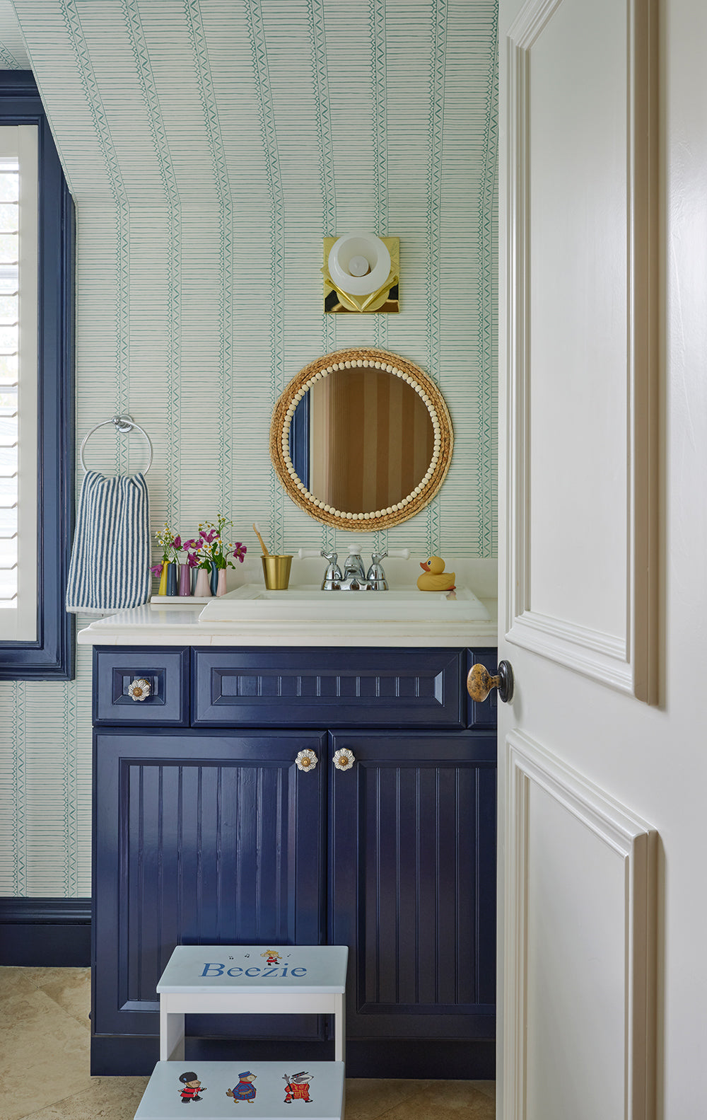 Navy vanity with a round mirror in a pale blue striped bathroom