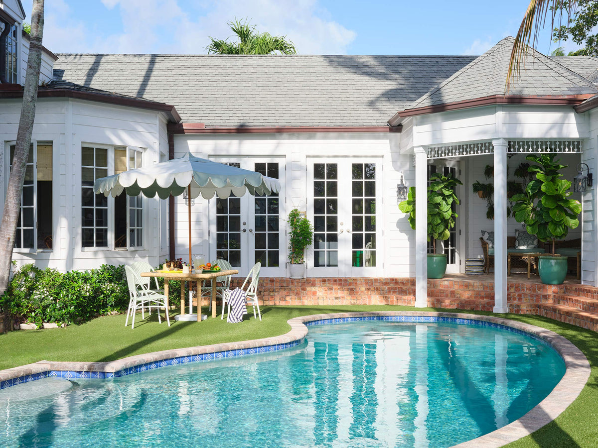 Pool terrace with a scalloped umbrella, lawn and the back of the white house