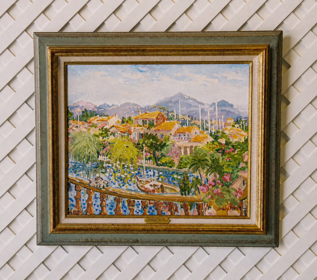 Front view of the framed Georges Flanet harbor painting on a white lattice wall