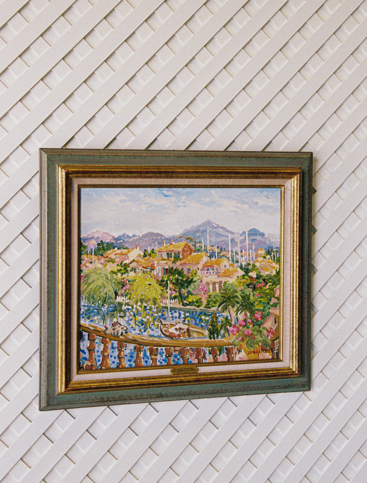Georges Flanet oil painting in a gilt and green frame, hung on a white lattice wall and seen from the side