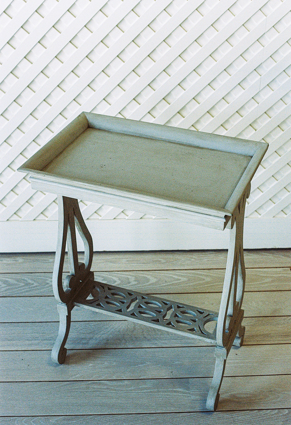 Gray washed side table with a tray top and a pierced lower shelf, from the side