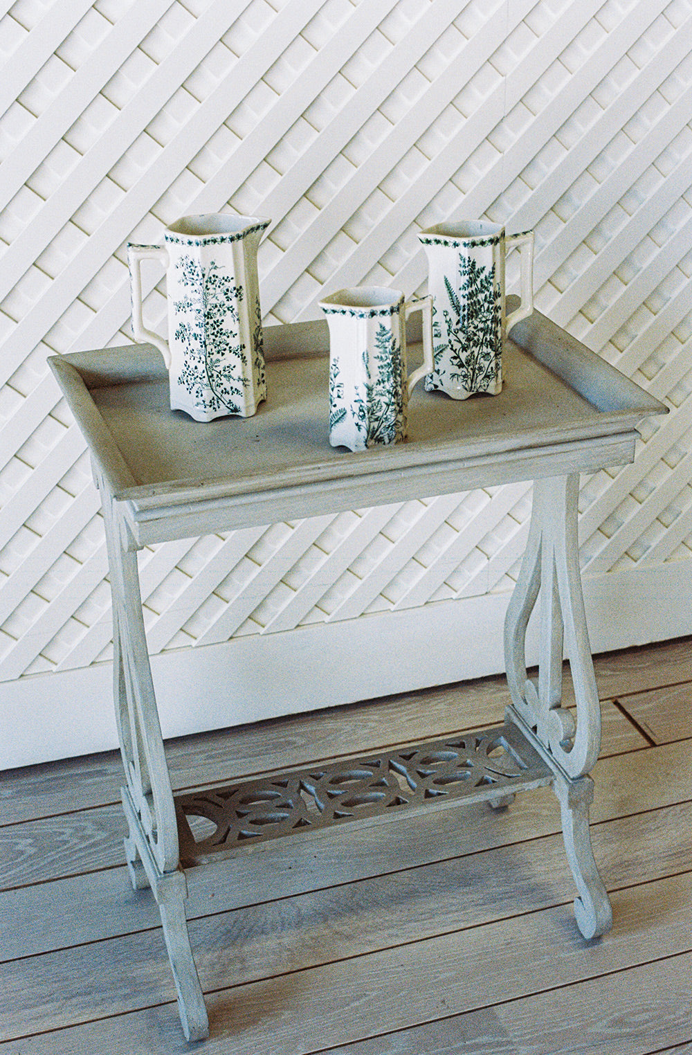 Gray washed side table with a tray top and a pierced lower shelf, from the side