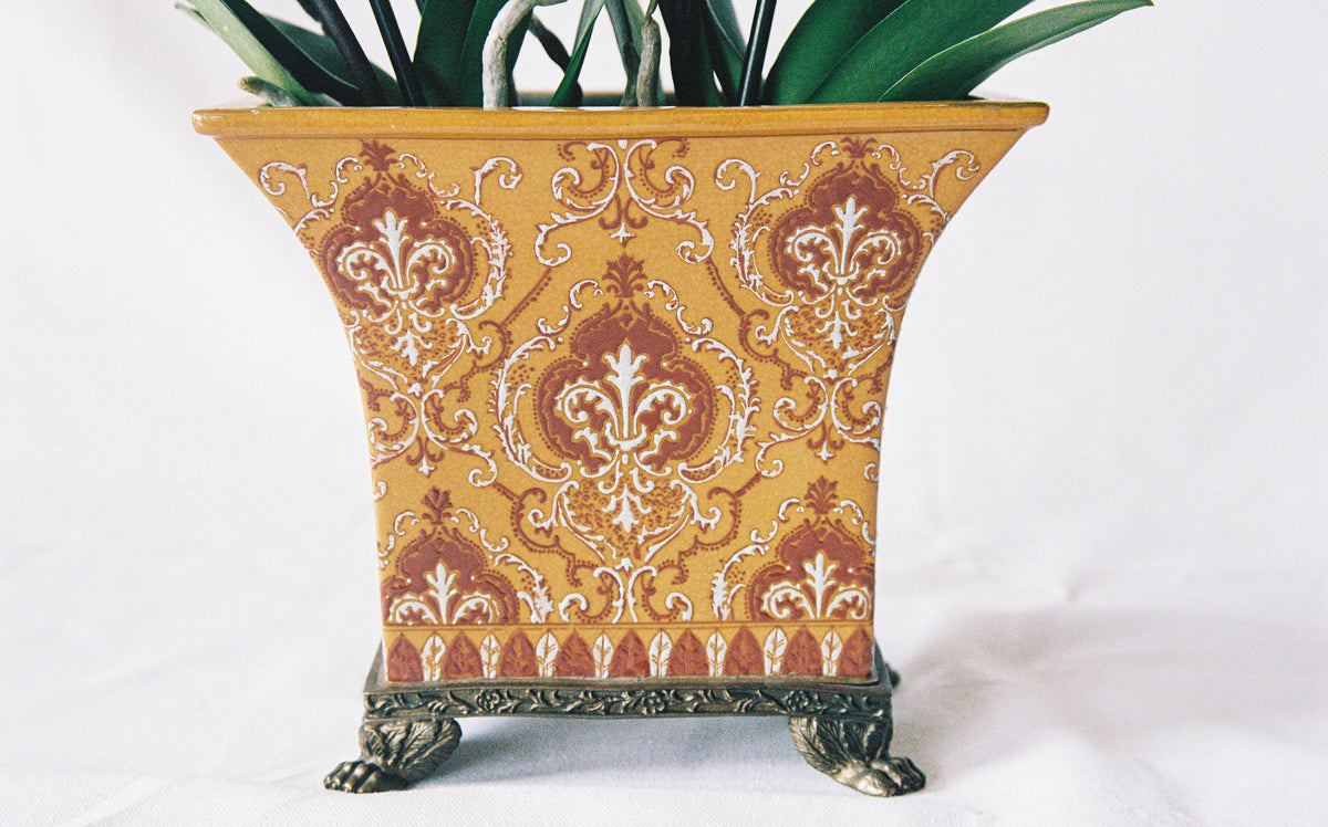 Ceramic cachepot with an ochre damask motif on an antiqued metal footed base, planted with an orchid