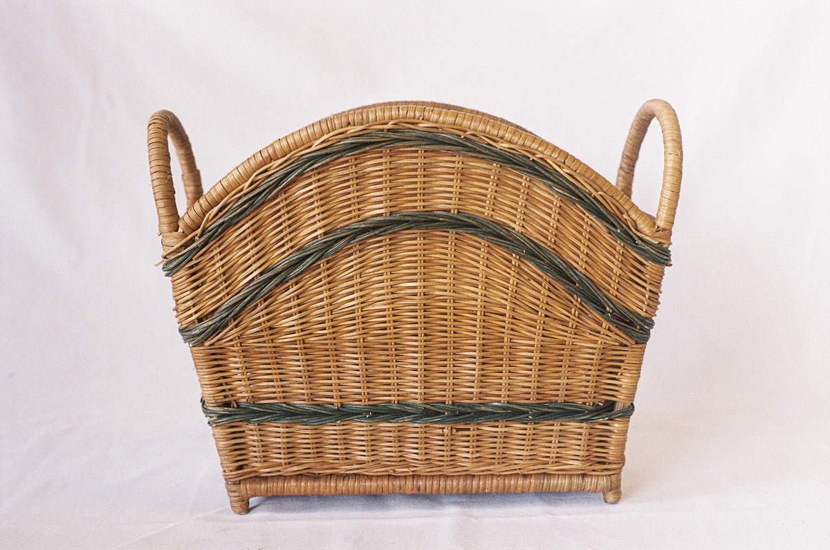 Natural wicker magazine holder with handles and green woven detailing, held for scale