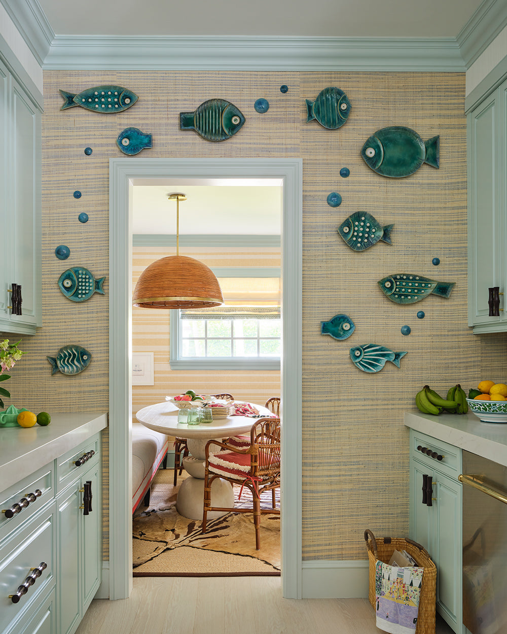 Pale blue kitchen hung with turquoise ceramic fish, looking through to a breakfast table