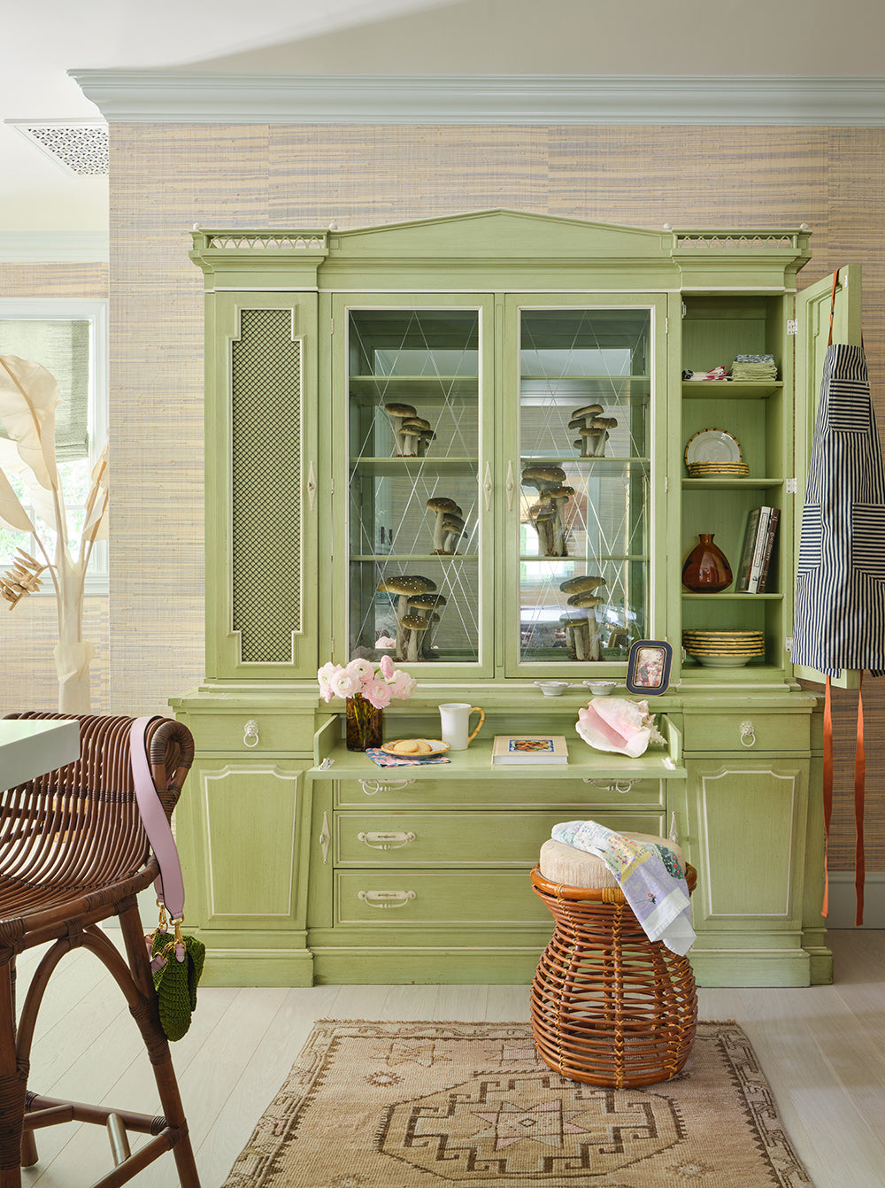 Pale green glazed hutch displaying shells and ceramics, with a rattan stool and a basket on a patterned rug