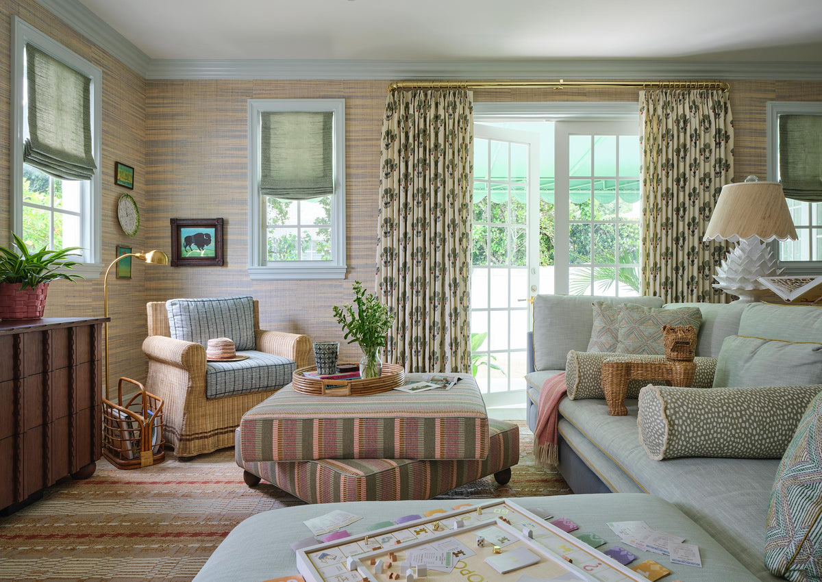 Family room with grasscloth walls, a striped ottoman, pale sofa and armchairs, and leaf print curtains at the windows