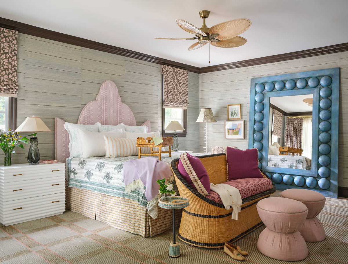 Girl's bedroom with a pink scalloped headboard, a blue shell framed mirror, a wicker chair and a pink upholstered stool