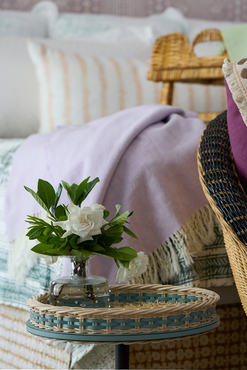 Still life of white roses on a blue beaded tray table, with a lilac throw over a woven chair