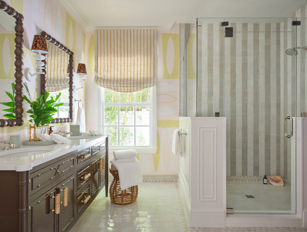 Bathroom with yellow patterned walls, a grey double vanity, a striped roman shade and a glass shower