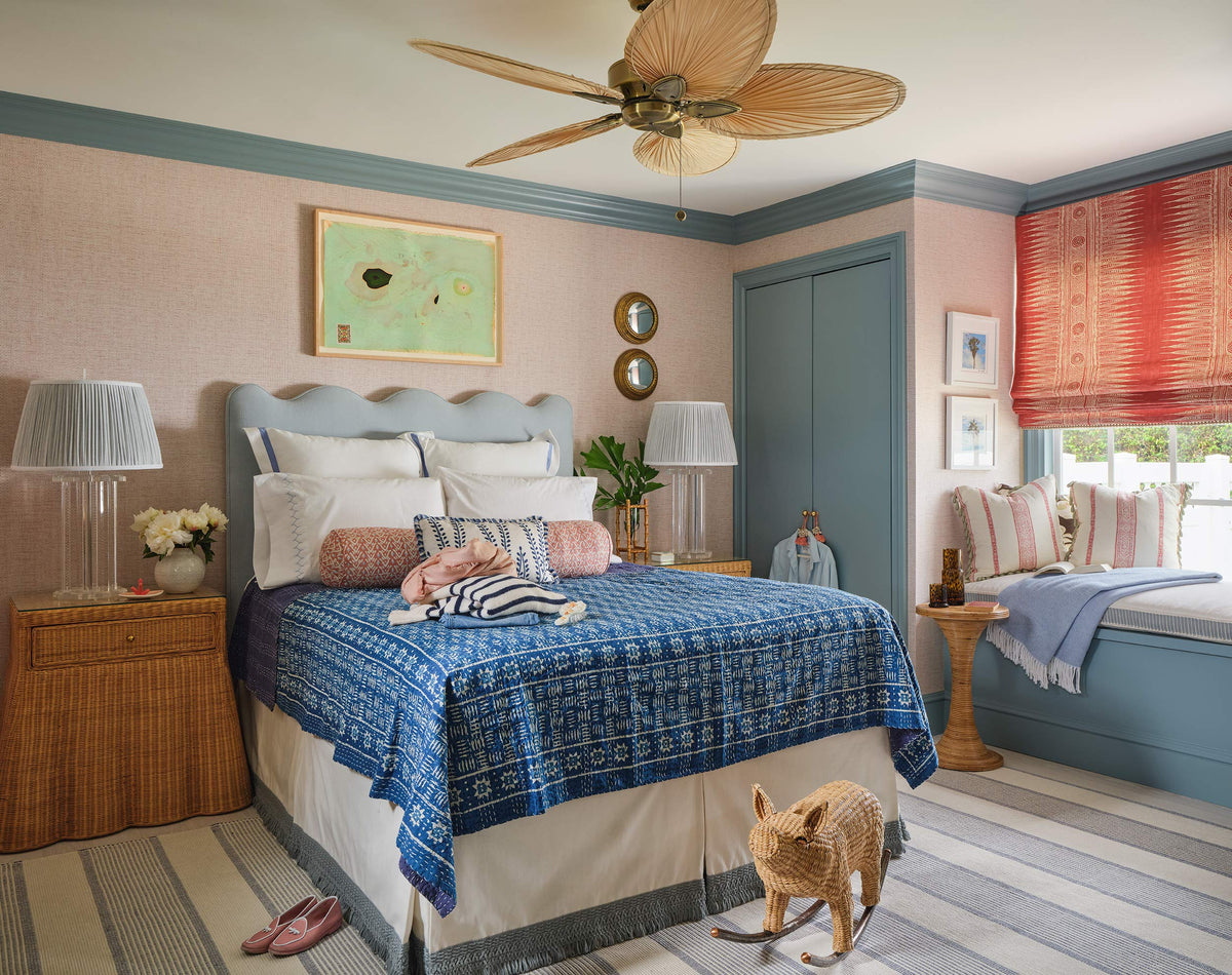 Bedroom with a scalloped blue headboard, indigo coverlet, coral roman shades and a striped rug, a dog on the floor