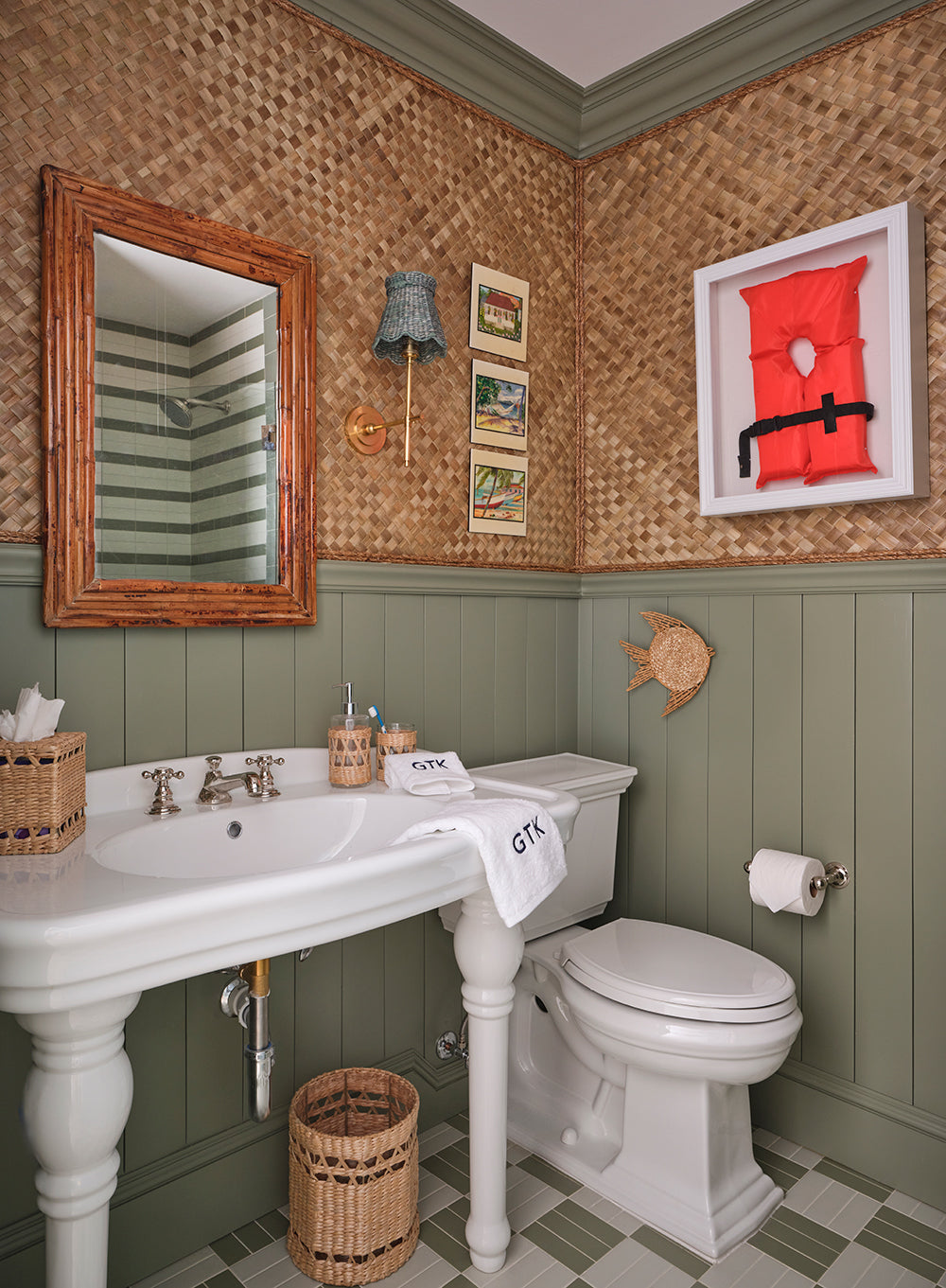 Powder room in woven raffia and sage panelling, with a pedestal basin, a rattan mirror and a red framed artwork