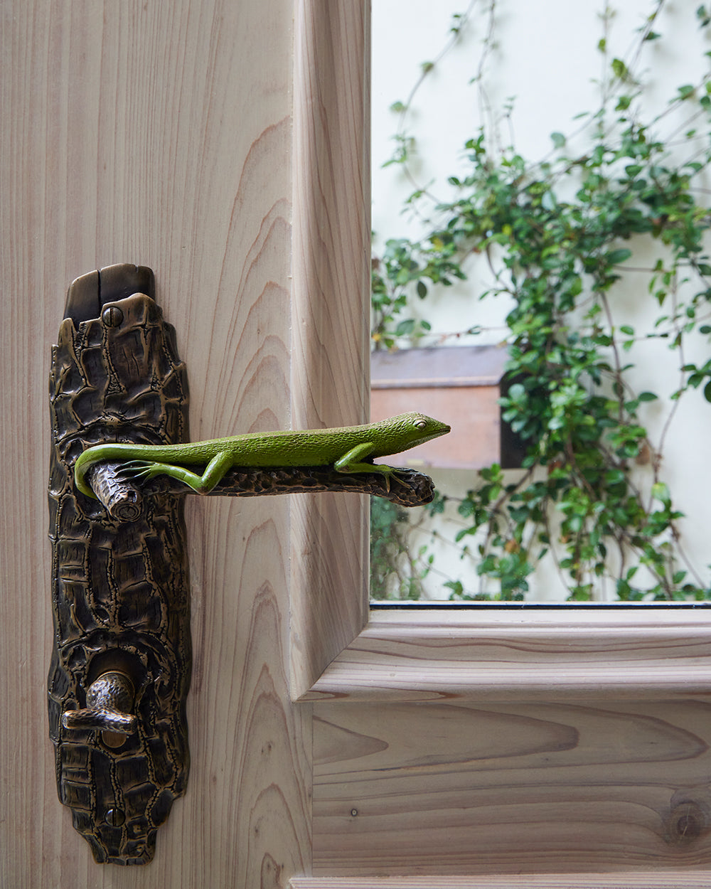 Door handle detail, a bronze python escutcheon with a green lizard lever on pale timber