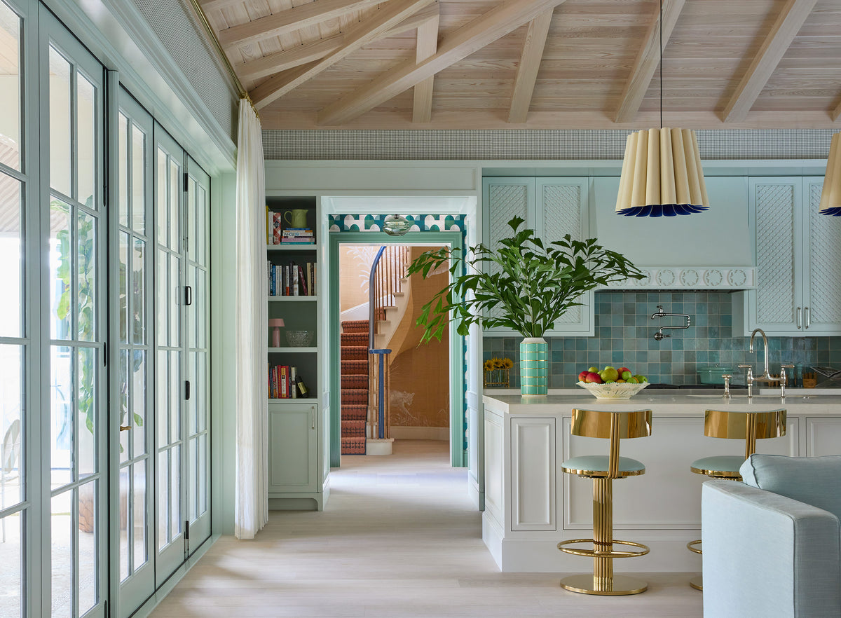 Kitchen seen through the sitting room, pale green cabinets, brass bar stools and a lemon tree on the island