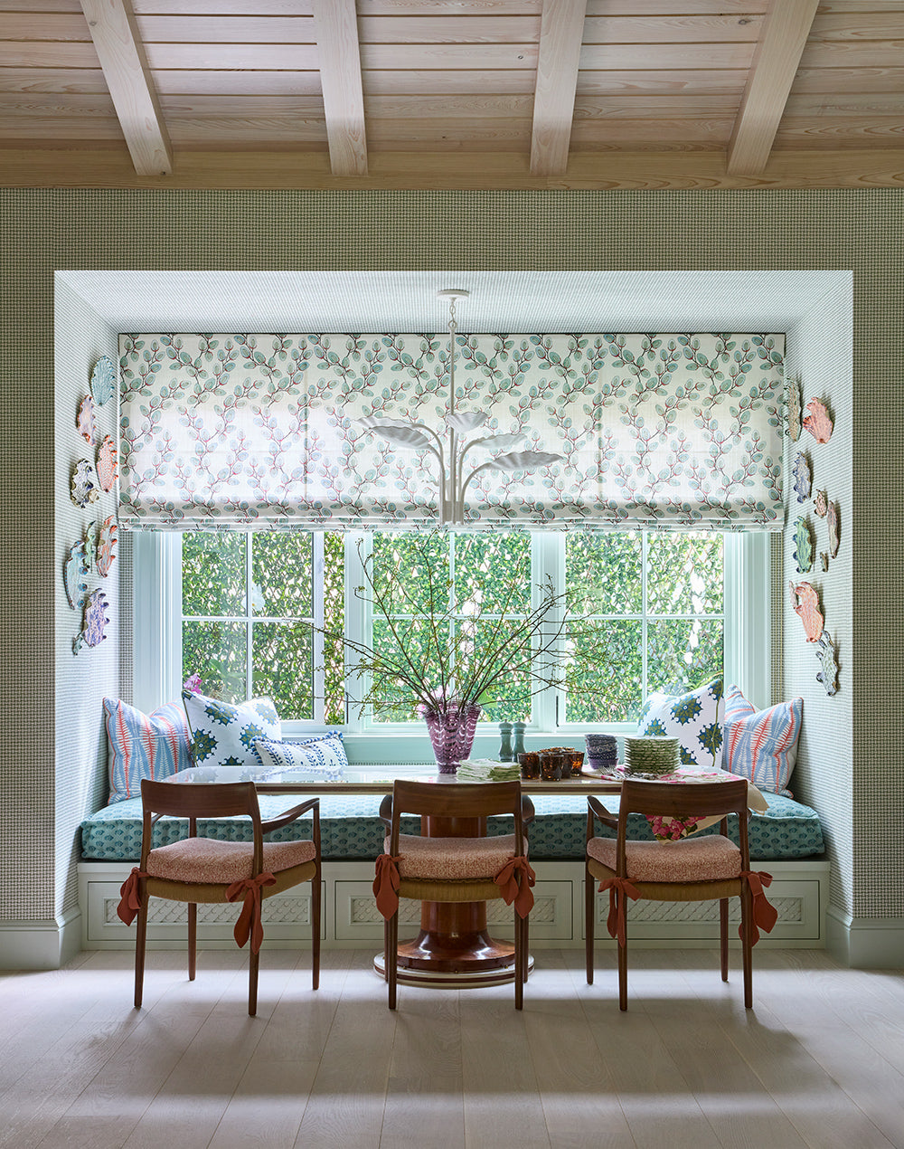 Window seat breakfast nook with a printed roman shade, a round table and antique chairs, shells on the wall