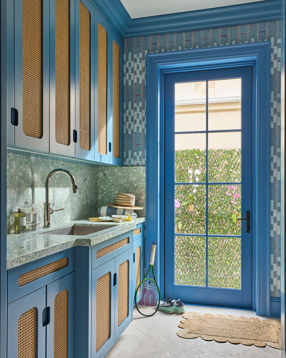 Blue cabinetry with caned fronts and a green trellis tiled splashback beside a glazed garden door