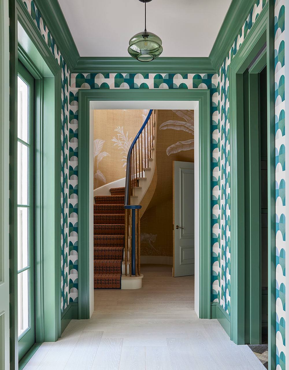 Corridor in green scallop patterned wallpaper looking through to a staircase with a painted palm mural