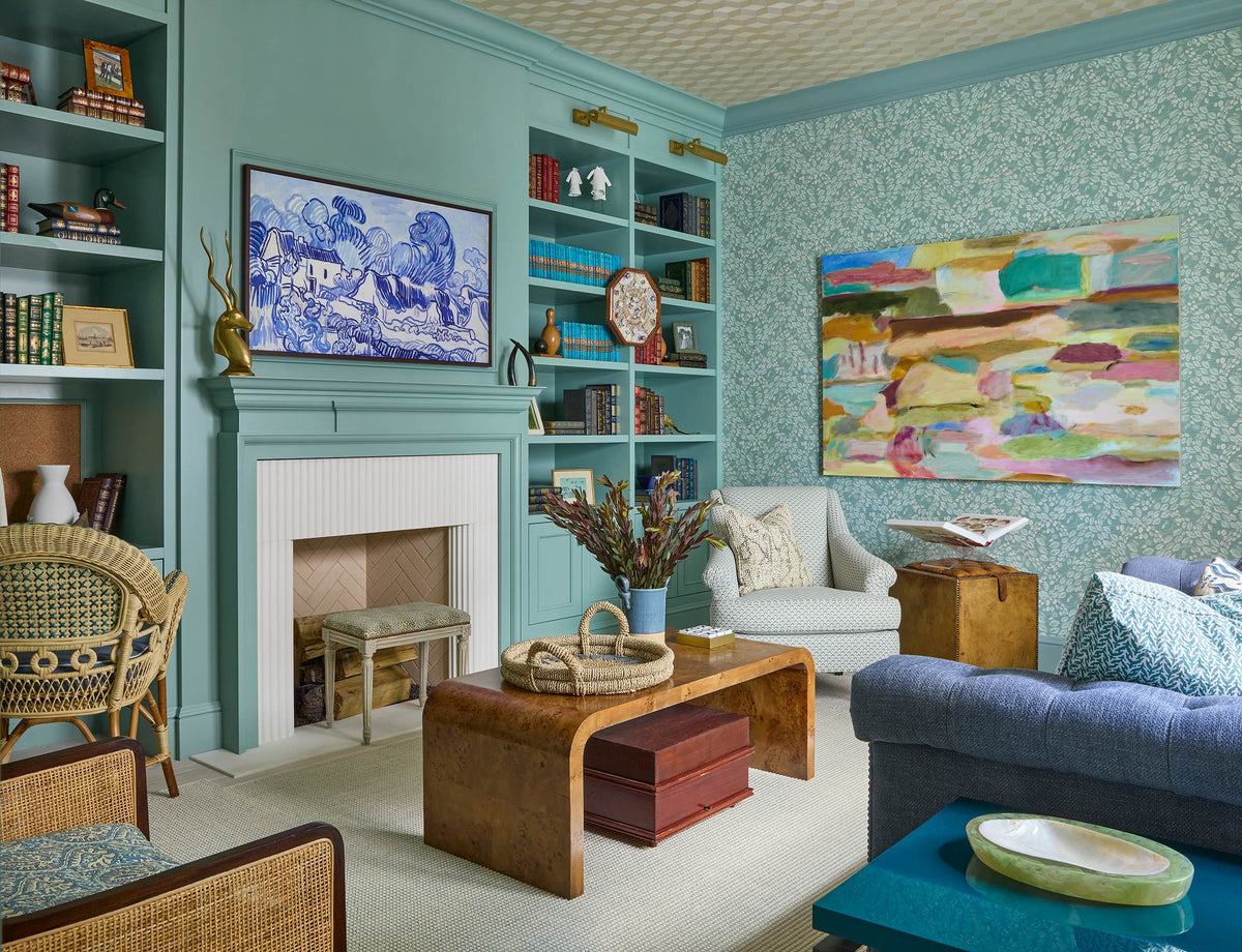 Living room in turquoise with built in shelves, a burl coffee table, a blue sofa and colourful art over the fireplace