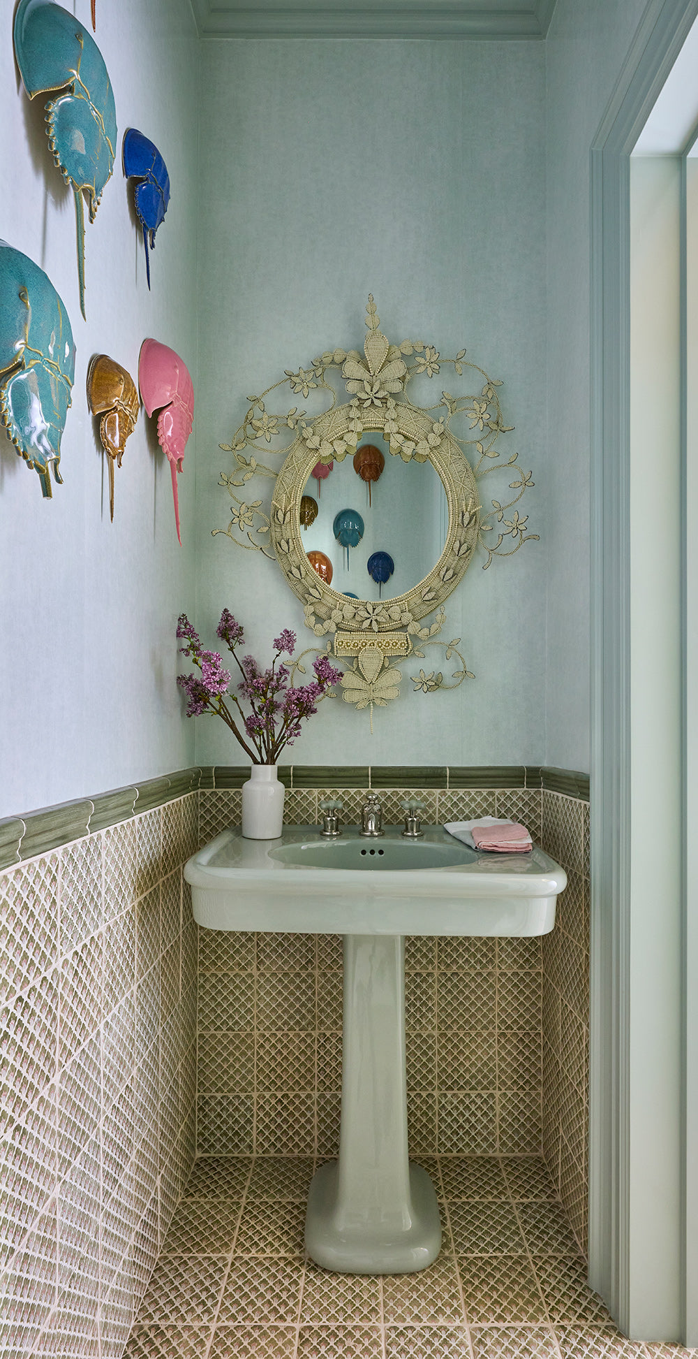 Powder room with a pedestal basin, a scalloped gilt mirror and turquoise ceramic shells on pale green walls