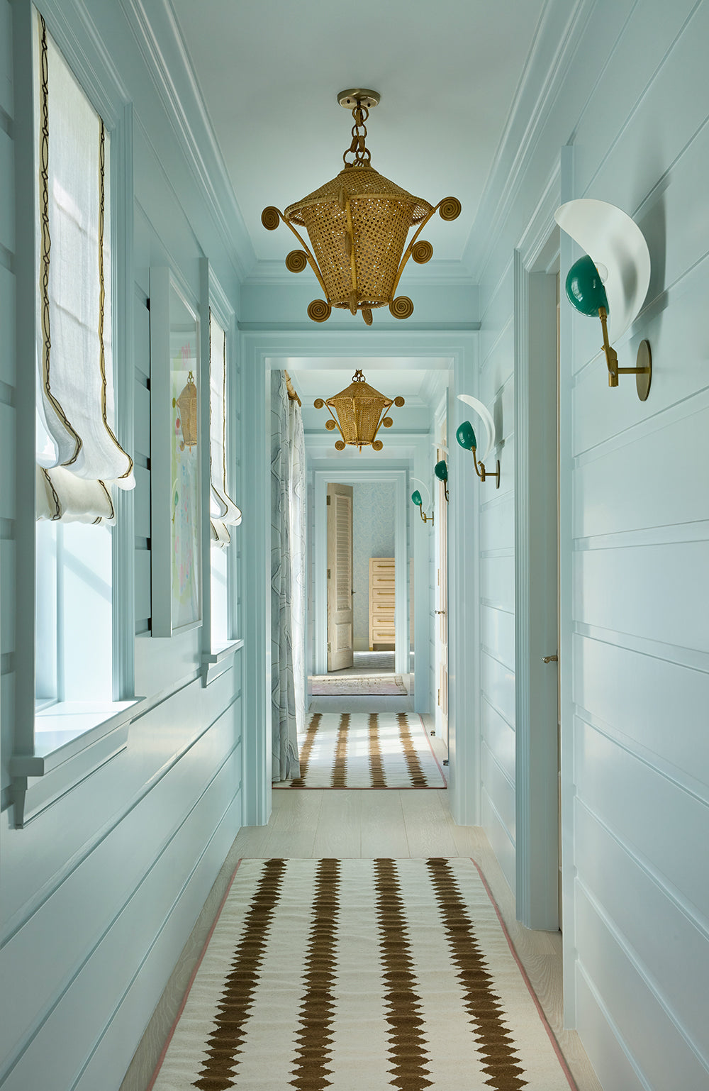 Pale blue corridor with a brass lantern, wall sconces and a striped runner