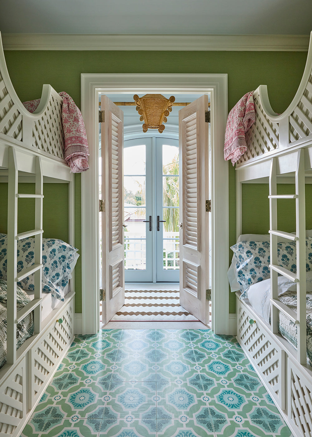 Bunk room with white fretwork bunks either side of a patterned tile floor, looking out to the garden
