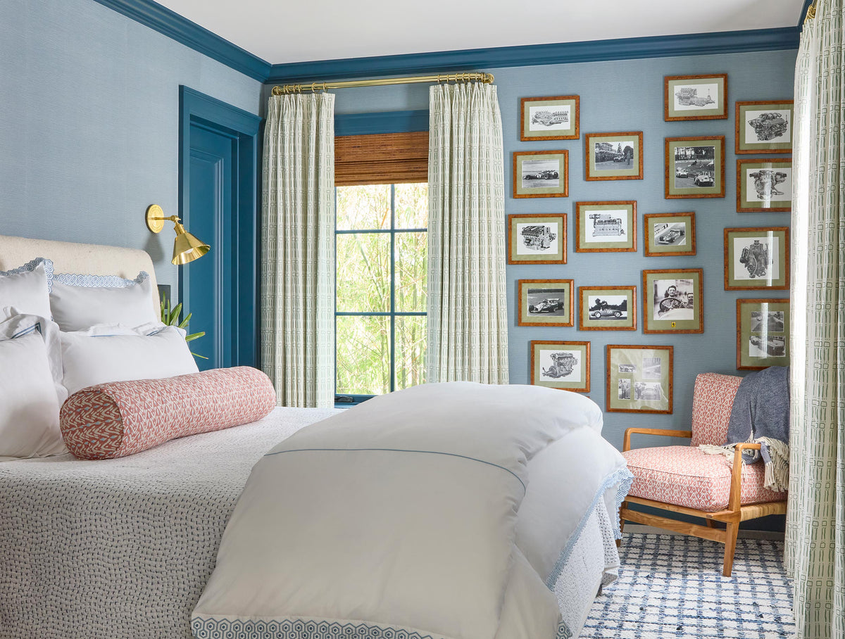 Blue bedroom with a gallery wall of framed prints, white bedding and a coral bolster