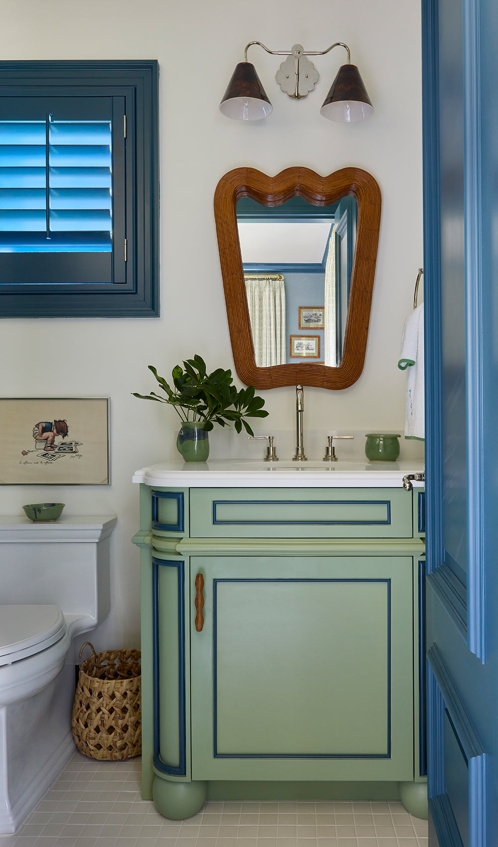 Bathroom with a green panelled vanity, a shaped gilt mirror and a blue shuttered window