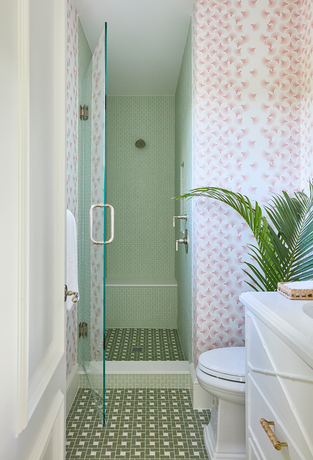 Shower room in green tile with pink patterned wallpaper and a potted palm