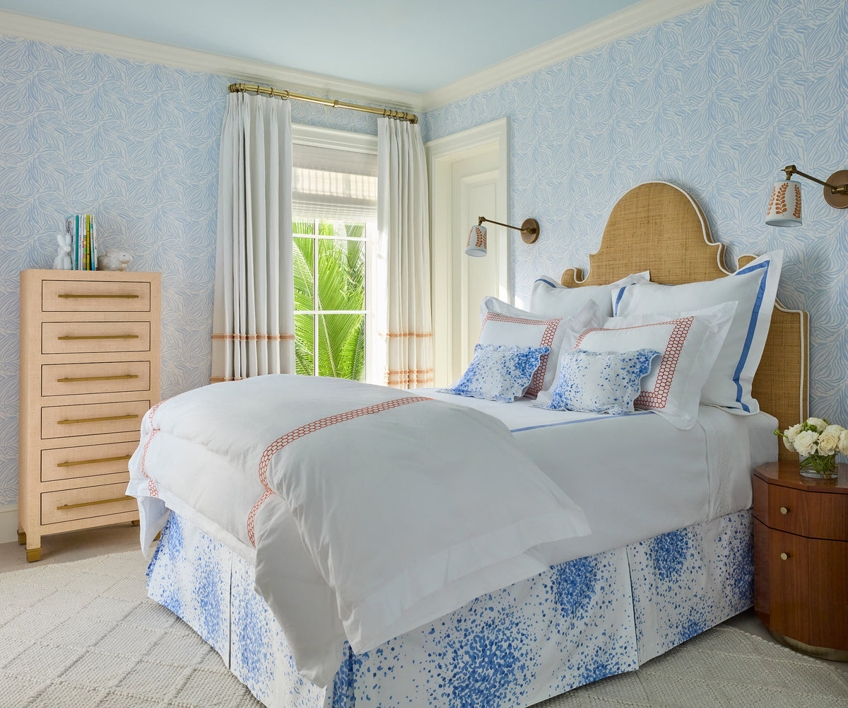 Bedroom with pale blue wallpaper, a caned headboard, a blue block print bed skirt and a limed chest