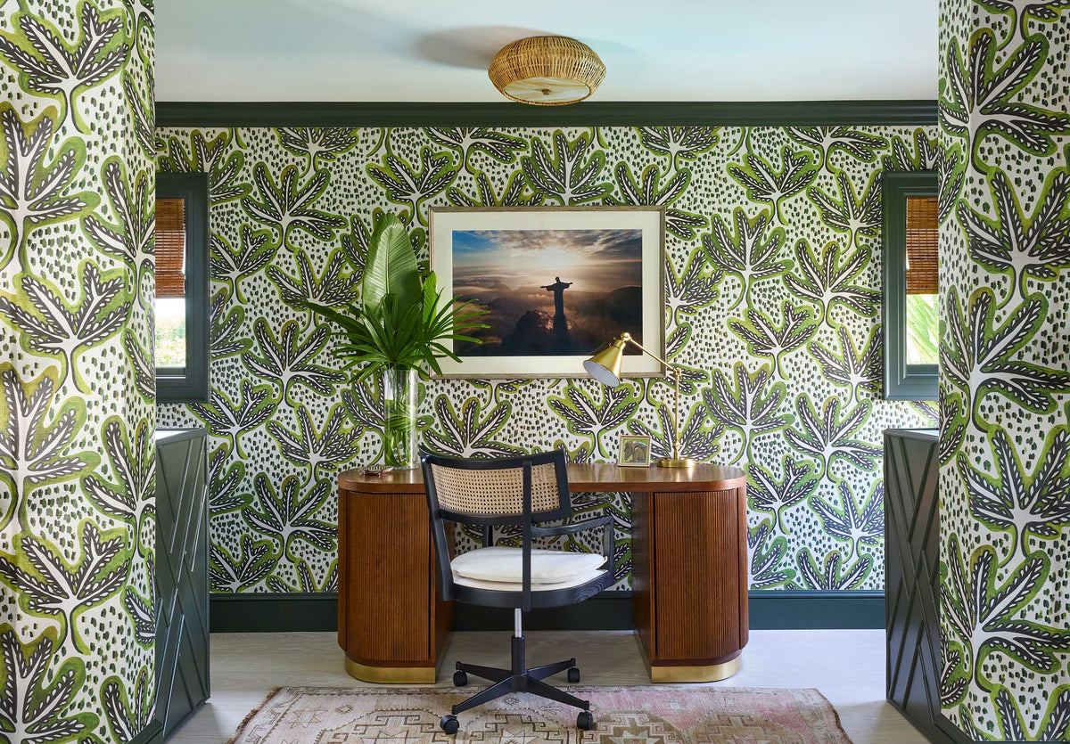 Study in green leaf wallpaper with a walnut desk, a caned chair and a framed sailing photograph