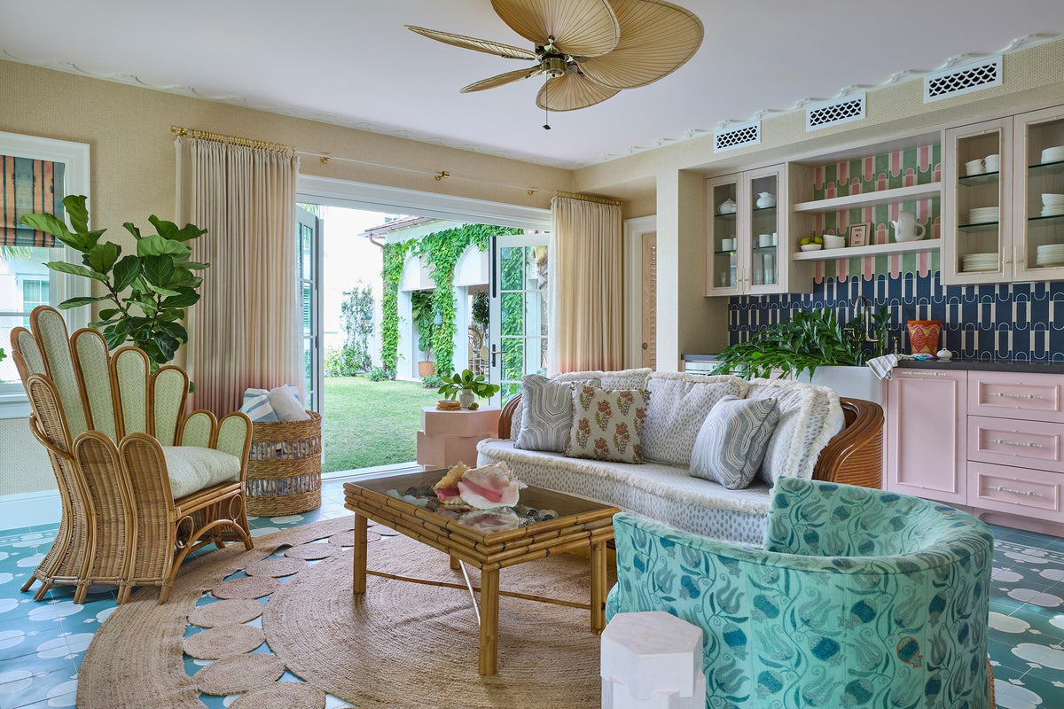 Family room with a rattan ceiling fan, a navy tiled kitchen beyond, turquoise patterned chairs and a woven rug