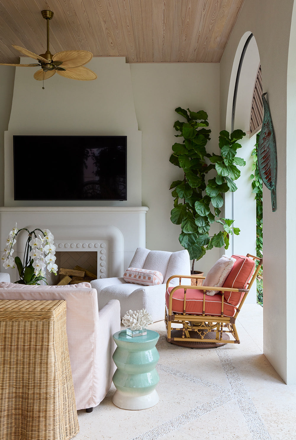 Covered loggia with a fireplace, white sofas, a coral striped rattan chair and a celadon garden stool