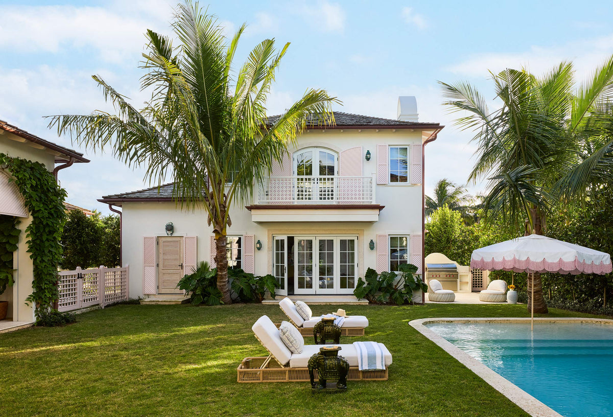 Pink house and lawn with palms, loungers and a striped umbrella beside the pool