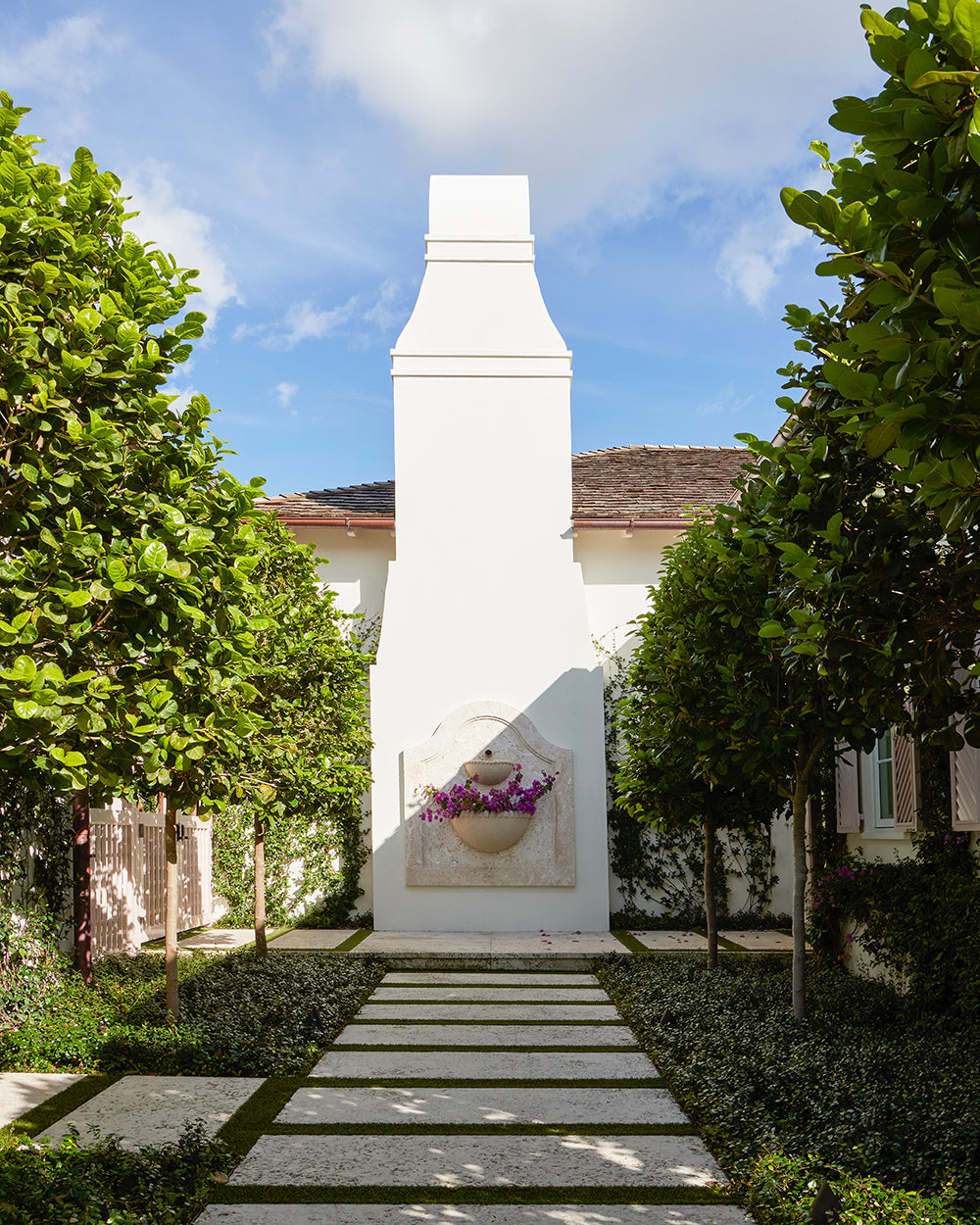 Garden path of stone pavers to a white chimney fountain flanked by clipped trees