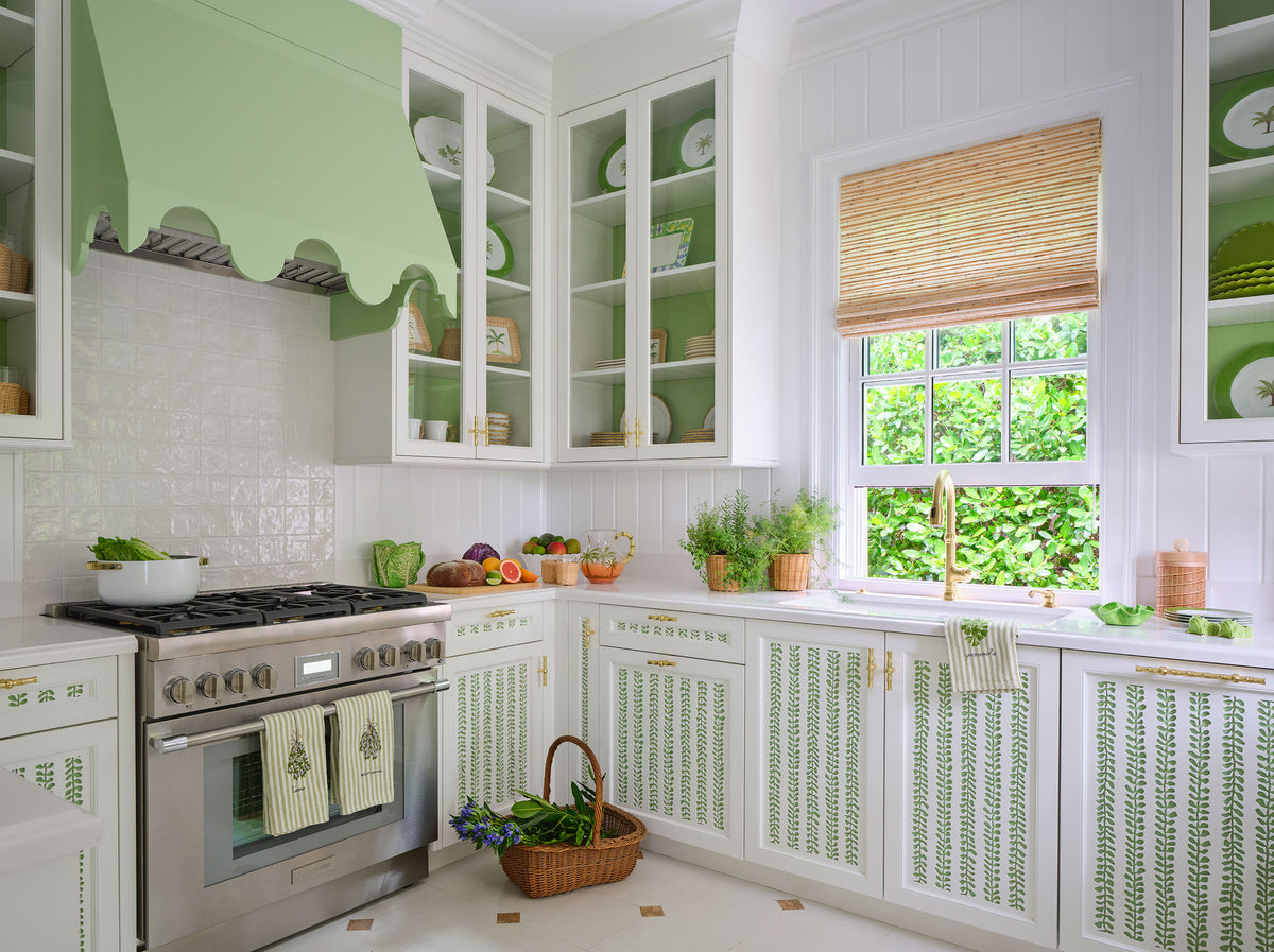 Kitchen with a scalloped green range hood, glazed cabinets, woven shades and green caned cabinet fronts