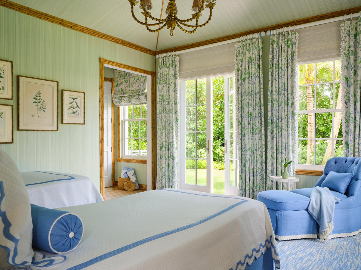 Bedroom in pale green panelling with a bamboo chandelier, botanical prints, leaf print curtains and blue bedding