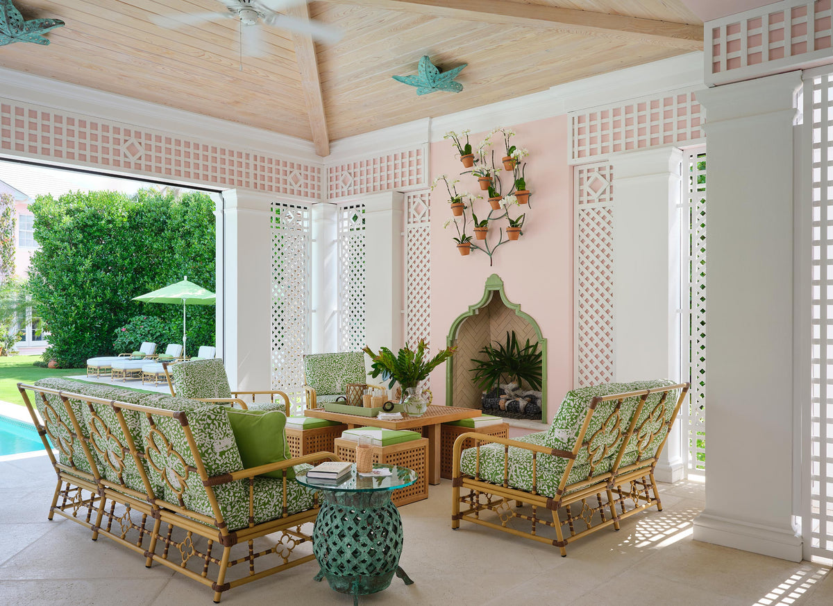 Loggia with a pink coffered ceiling and lattice walls, green patterned rattan seating and a ceramic garden stool by the pool