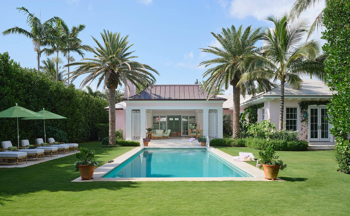 Pool and lawn framed by palms, with a pink pavilion and loungers under green umbrellas