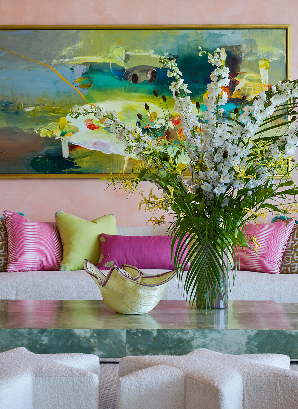 Sofa detail below a green and turquoise abstract, magenta and chartreuse cushions and a tall white orchid arrangement