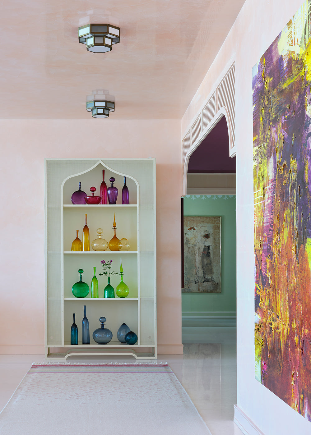 Blush corridor with a fretwork niche of coloured glass bottles and a large abstract canvas
